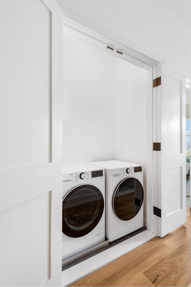 clothes washing area with washing machine and clothes dryer and wood finished floors