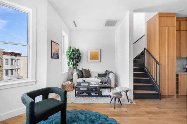 sitting room with stairway, light wood-style floors, visible vents, and baseboards