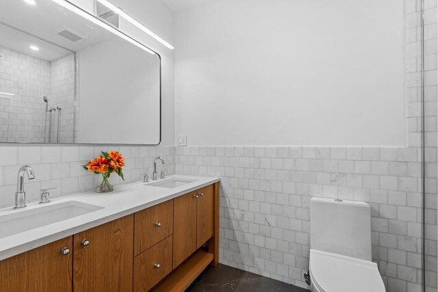 full bathroom with tile walls, marble look tile flooring, toilet, tiled shower, and a wainscoted wall
