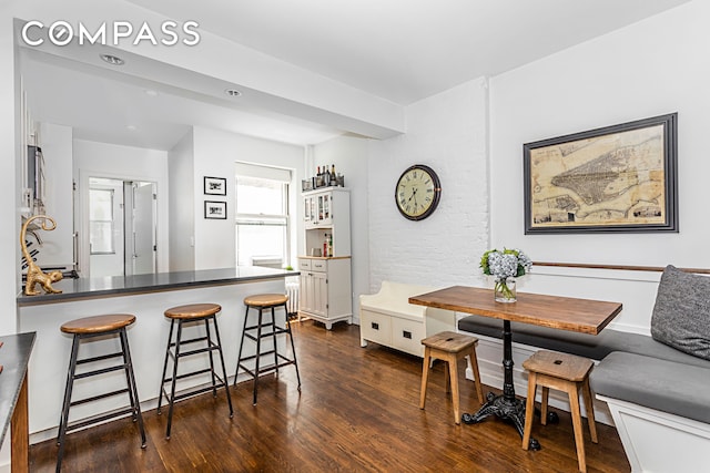 kitchen featuring a kitchen bar, dark countertops, white cabinetry, a peninsula, and dark wood-style flooring