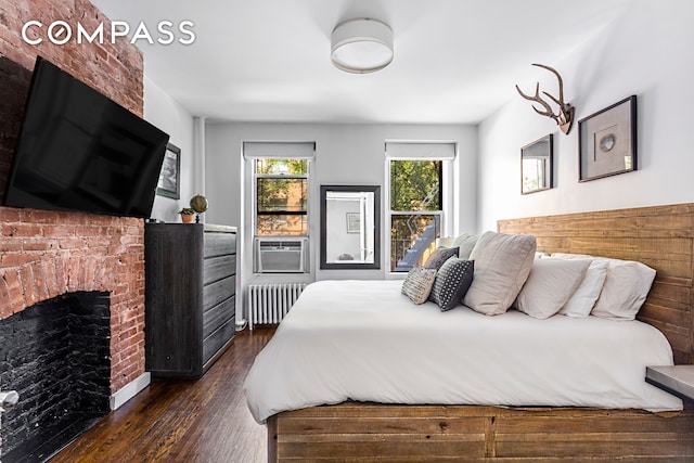 bedroom with dark wood-style floors, cooling unit, a brick fireplace, and radiator heating unit