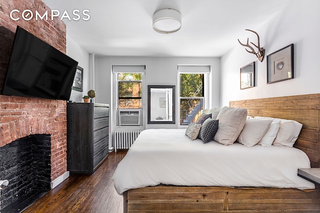bedroom with a brick fireplace, dark wood-style flooring, cooling unit, and radiator