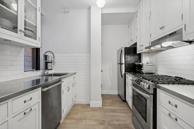 kitchen featuring light wood finished floors, appliances with stainless steel finishes, white cabinets, a sink, and under cabinet range hood