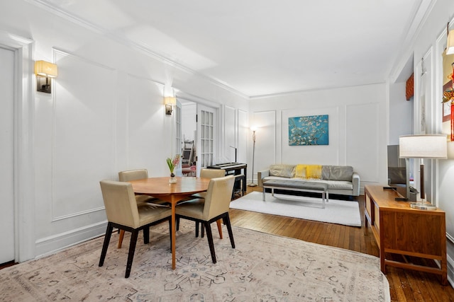 dining room with ornamental molding, a decorative wall, and hardwood / wood-style floors