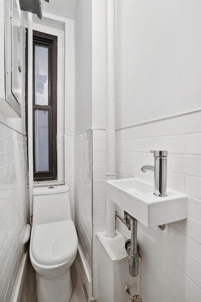 half bathroom featuring toilet, a sink, tile walls, and wainscoting