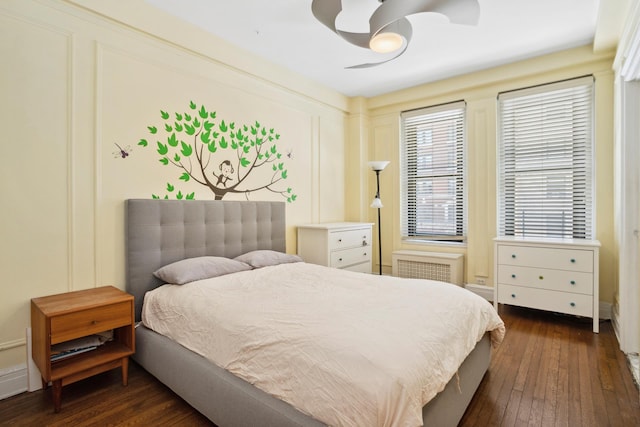 bedroom with ceiling fan, radiator heating unit, dark wood finished floors, and a decorative wall