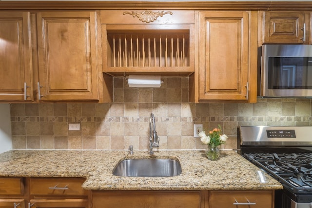 kitchen with stainless steel appliances, backsplash, a sink, and brown cabinets