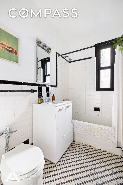 full bathroom with shower / bath combo, tile walls, vanity, and toilet