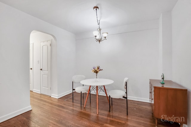 dining area featuring arched walkways, a chandelier, wood finished floors, and baseboards