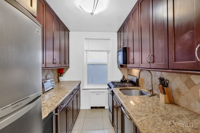 kitchen featuring reddish brown cabinets, light tile patterned floors, stainless steel appliances, a sink, and light stone countertops