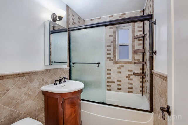 full bath with wainscoting, toilet, enclosed tub / shower combo, vanity, and tile walls