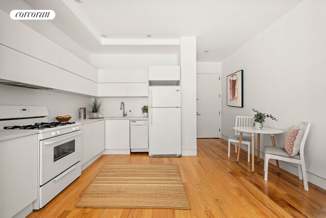 kitchen with white appliances, white cabinets, light countertops, light wood finished floors, and modern cabinets