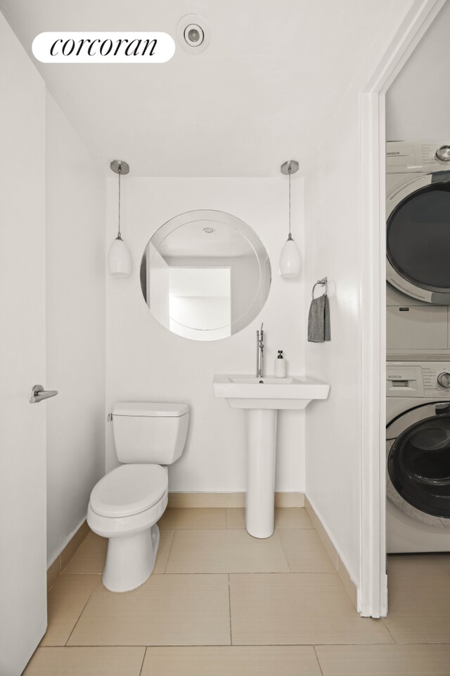 bathroom featuring stacked washer / dryer, tile patterned flooring, toilet, and baseboards