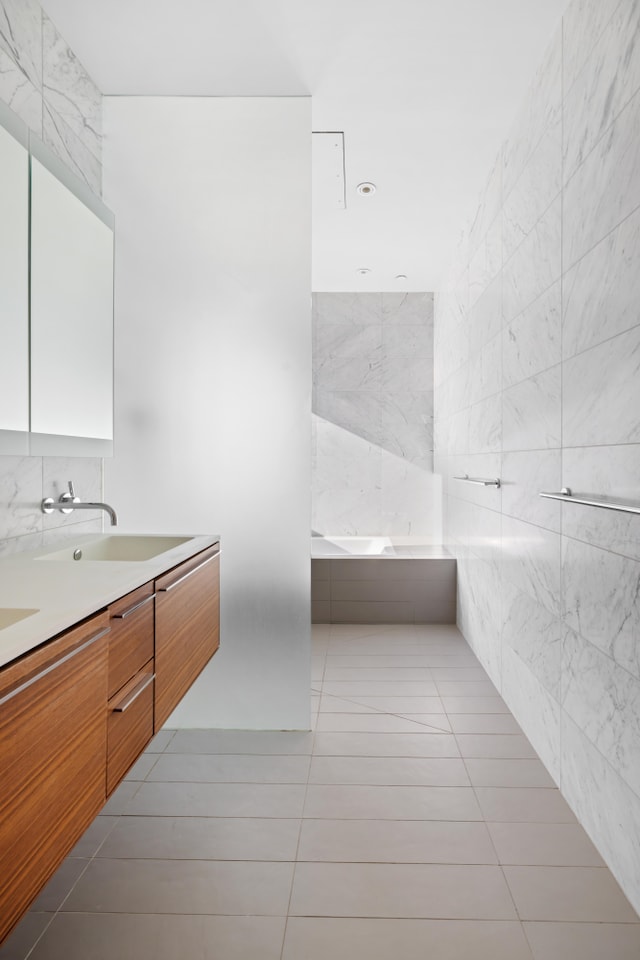 bathroom featuring double vanity, a sink, a garden tub, tile patterned flooring, and tile walls