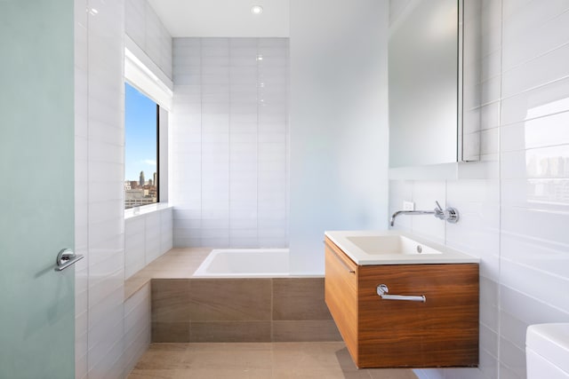 bathroom featuring tile walls, tiled bath, toilet, vanity, and tile patterned floors