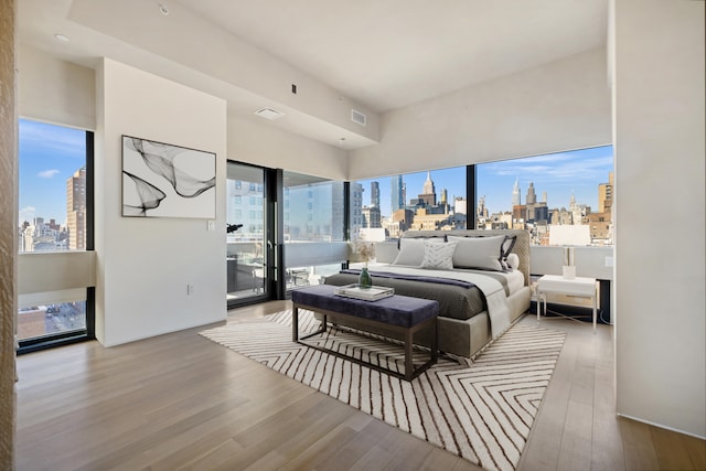 bedroom with access to exterior, a city view, visible vents, and wood finished floors