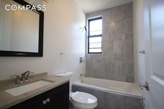 full bathroom featuring tiled shower / bath, tile walls, vanity, and toilet