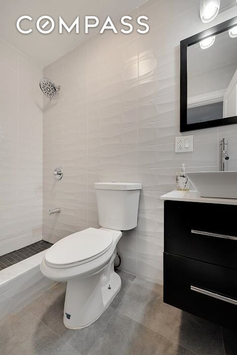 bathroom featuring vanity, toilet, tiled shower, and tile walls