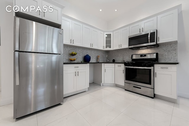 kitchen featuring dark countertops, backsplash, stainless steel appliances, and white cabinetry