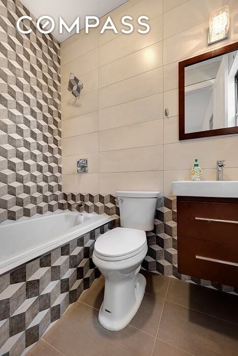 bathroom featuring tile patterned flooring, tile walls, vanity, tiled bath, and toilet