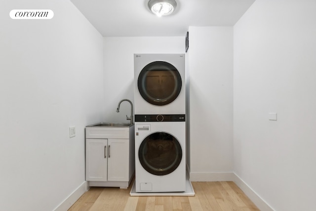 laundry room featuring stacked washer and dryer, a sink, cabinet space, light wood-style floors, and baseboards