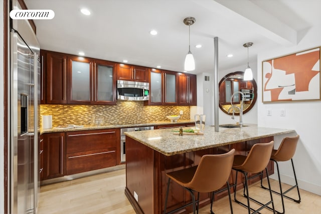 kitchen featuring light wood-type flooring, a breakfast bar, stainless steel appliances, decorative backsplash, and hanging light fixtures