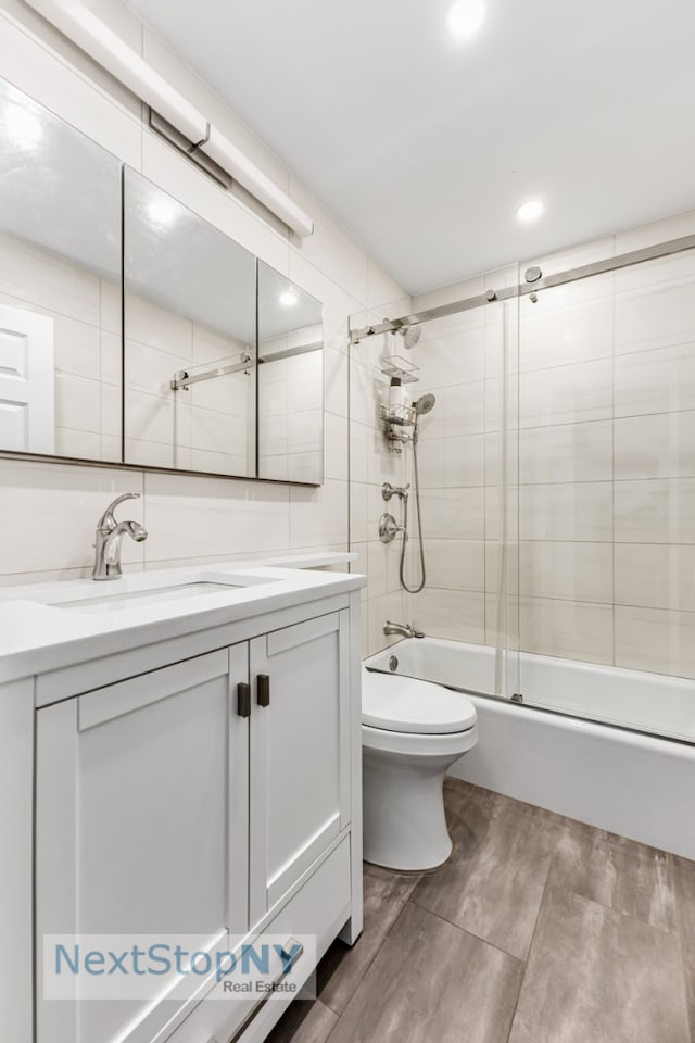 full bath featuring toilet, bath / shower combo with glass door, wood finished floors, vanity, and tile walls