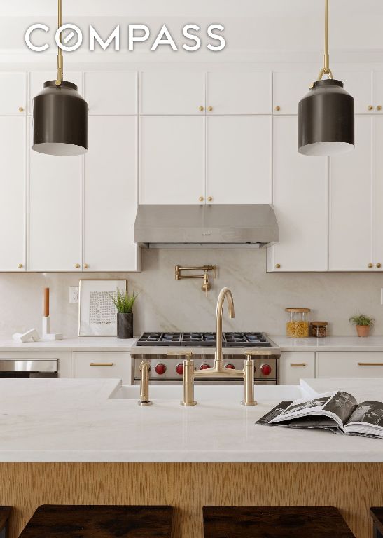 kitchen featuring under cabinet range hood, white cabinetry, light countertops, hanging light fixtures, and backsplash