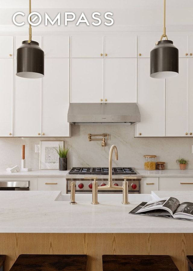 kitchen with under cabinet range hood, a kitchen bar, white cabinetry, and light countertops