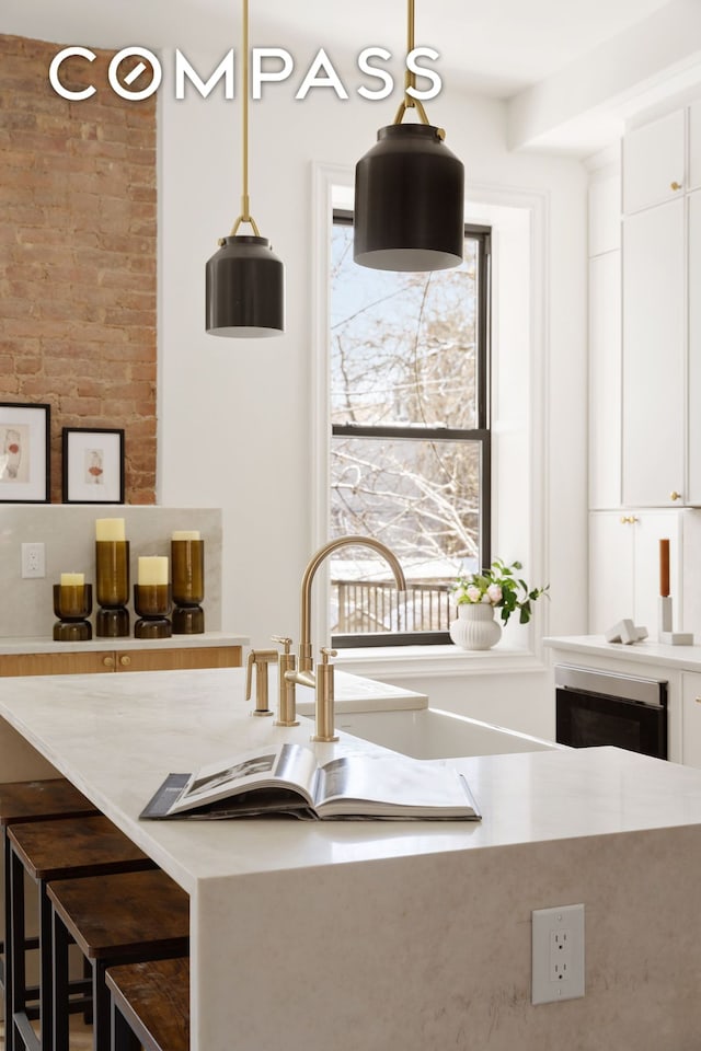 kitchen with hanging light fixtures, light countertops, white cabinets, and a sink