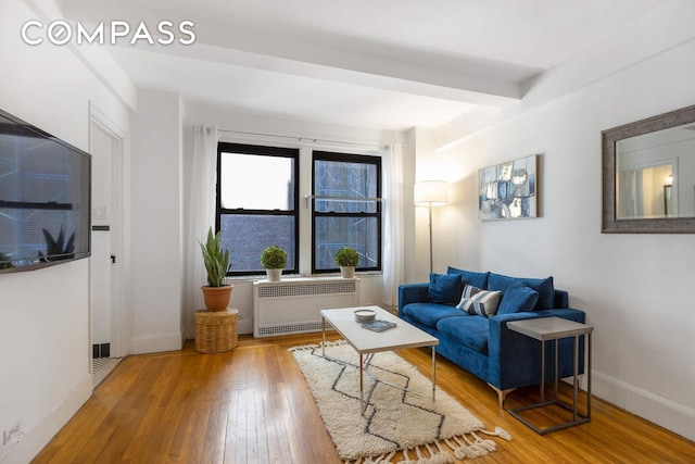 living area featuring hardwood / wood-style floors, beamed ceiling, radiator heating unit, and baseboards