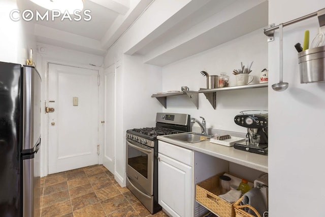kitchen with open shelves, appliances with stainless steel finishes, a sink, stone finish floor, and white cabinetry