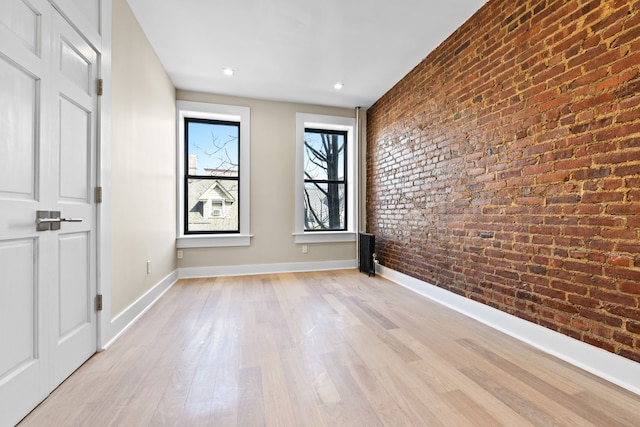 spare room featuring brick wall, light wood-type flooring, and baseboards