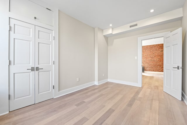 empty room featuring light wood-style flooring, recessed lighting, brick wall, visible vents, and baseboards