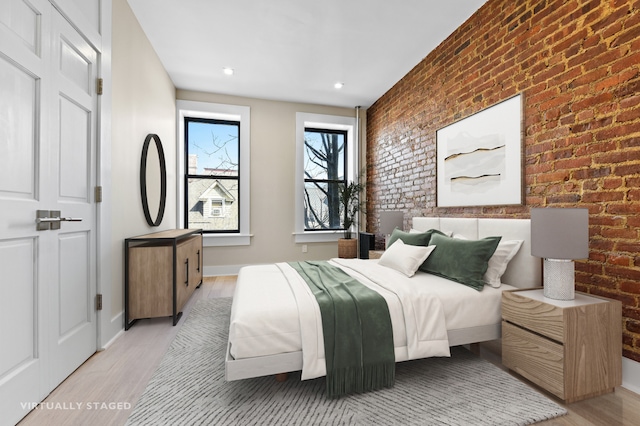 bedroom with light wood-type flooring, baseboards, and brick wall