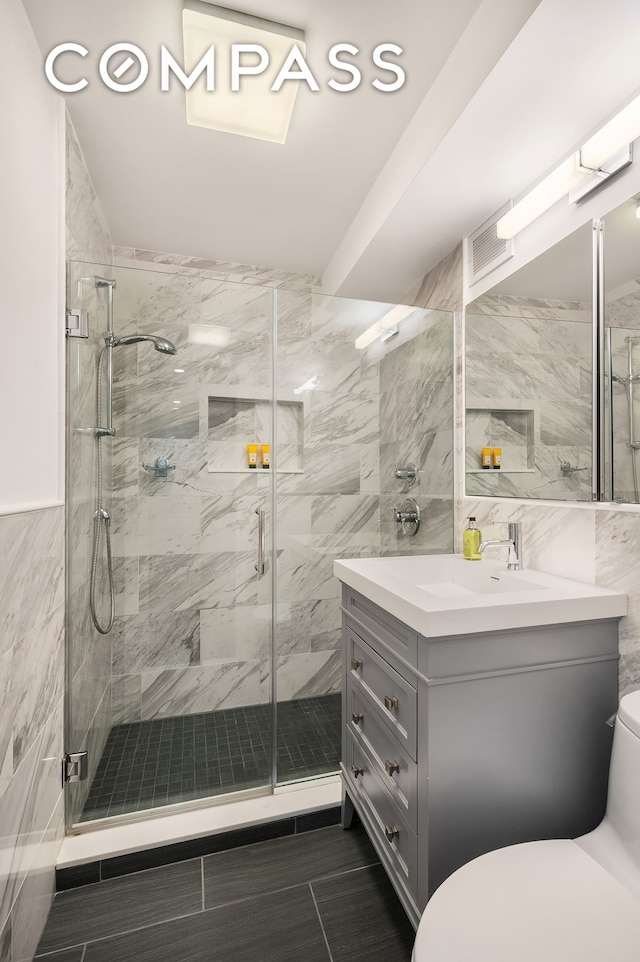 bathroom featuring tile walls, visible vents, toilet, a stall shower, and vanity