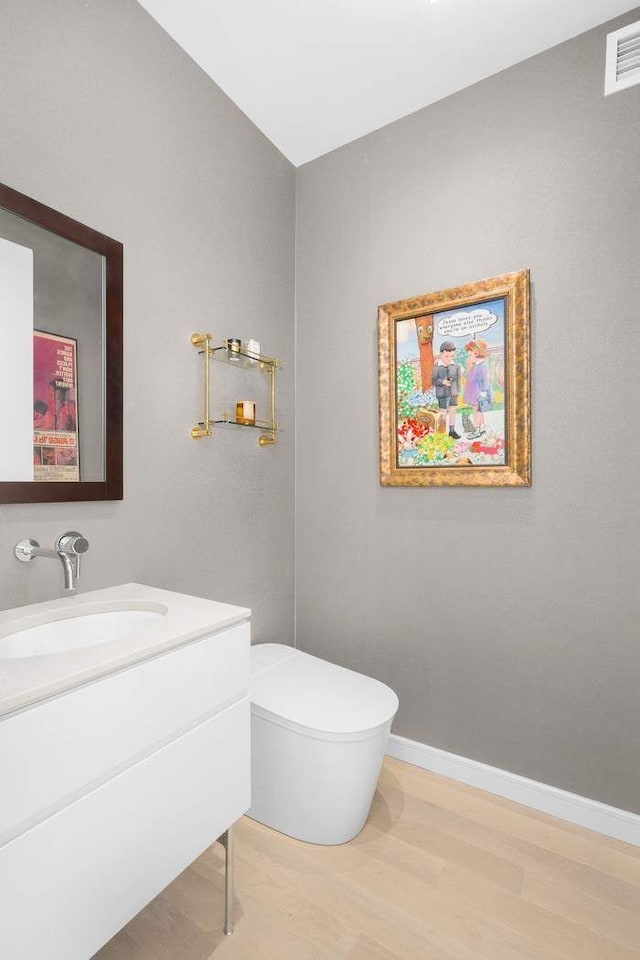 bathroom with vanity, wood finished floors, baseboards, visible vents, and toilet