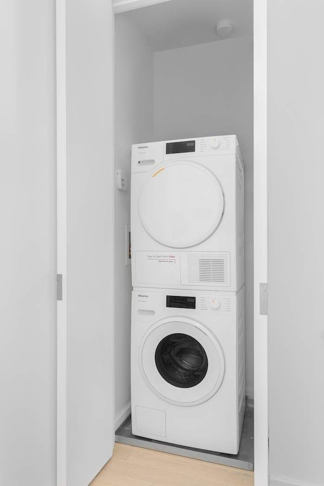 washroom featuring laundry area, stacked washer / drying machine, and wood finished floors