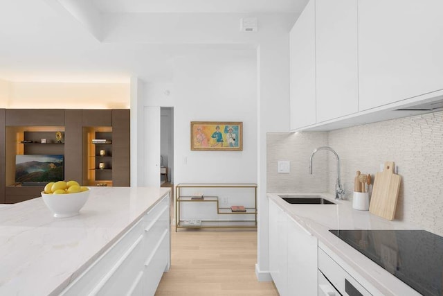 kitchen featuring black electric stovetop, light stone countertops, white cabinets, modern cabinets, and a sink