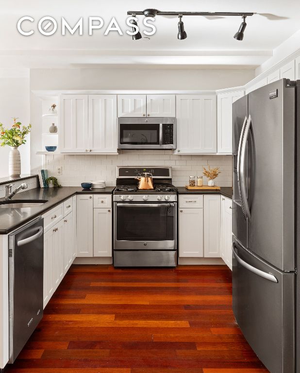 kitchen featuring tasteful backsplash, white cabinetry, sink, stainless steel appliances, and dark wood-type flooring