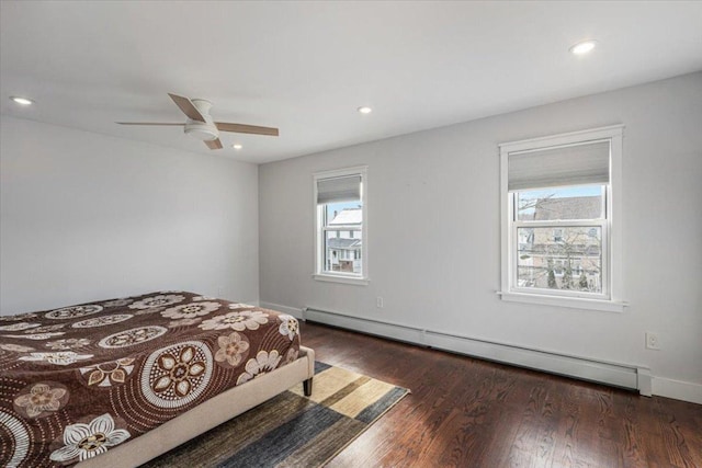 bedroom with ceiling fan, dark hardwood / wood-style floors, and a baseboard heating unit