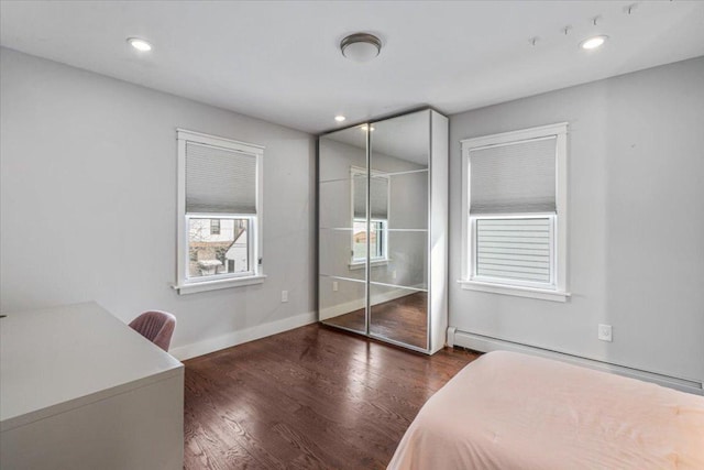 bedroom with a baseboard heating unit, dark hardwood / wood-style flooring, and a closet