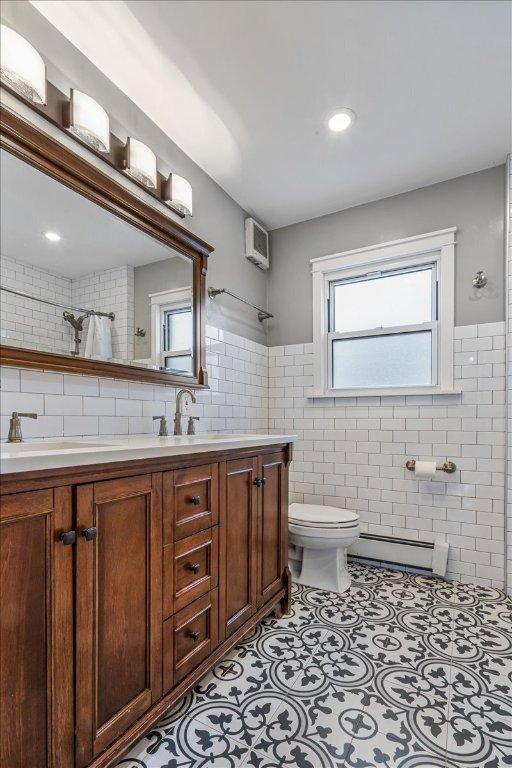 bathroom with baseboard heating, tile walls, vanity, tile patterned floors, and toilet