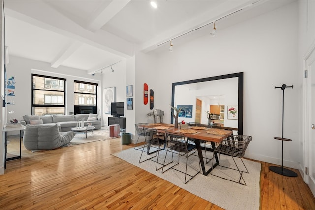 dining area with track lighting, beamed ceiling, baseboards, and wood-type flooring