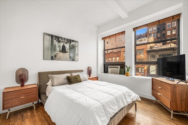 bedroom with cooling unit, beam ceiling, multiple windows, and hardwood / wood-style flooring