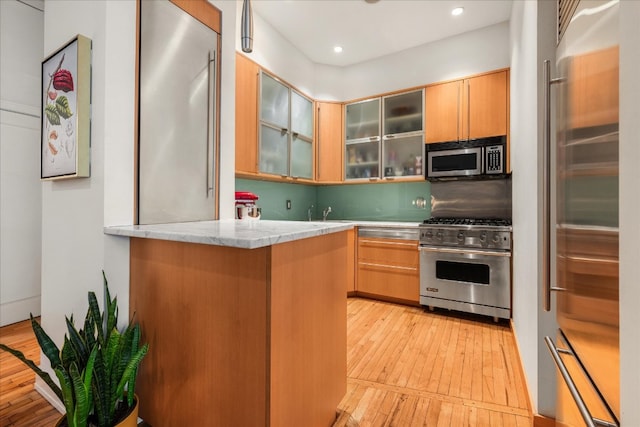 kitchen featuring a peninsula, light wood-style flooring, recessed lighting, glass insert cabinets, and high quality appliances