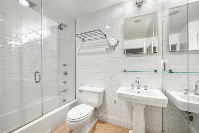 bathroom with tasteful backsplash, toilet, shower / bath combination with glass door, tile walls, and a sink