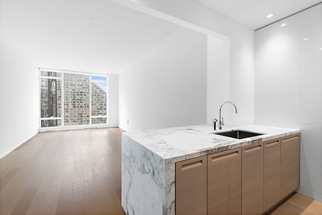 kitchen featuring floor to ceiling windows, sink, light stone counters, light wood-type flooring, and kitchen peninsula