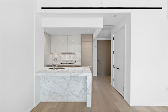 kitchen with sink, white cabinetry, light wood-type flooring, gas cooktop, and decorative backsplash