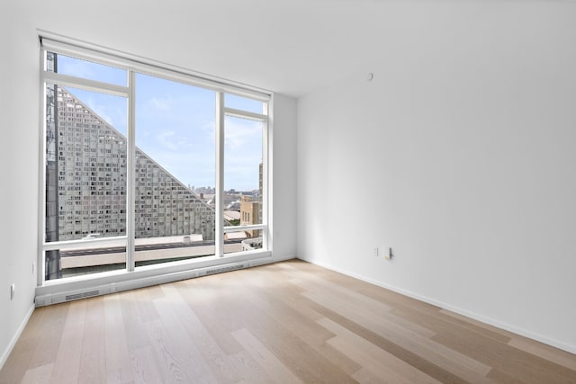 unfurnished room featuring a wall of windows and light hardwood / wood-style flooring